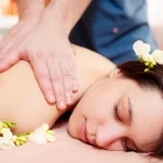 Massage therapist applying gentle pressure to client’s back in quiet treatment room